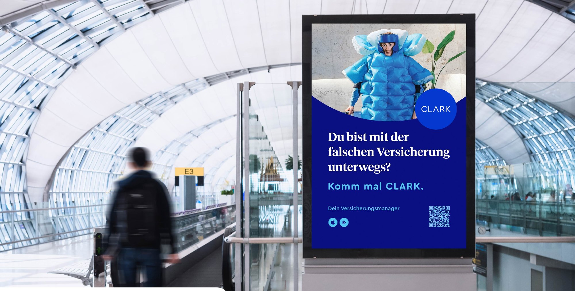 Komm mal CLARK — a digital out-of-home screen in an airport showing an over-protected traveller and the line 'Du bist mit der falschen Versicherung unterwegs? Komm mal CLARK.'