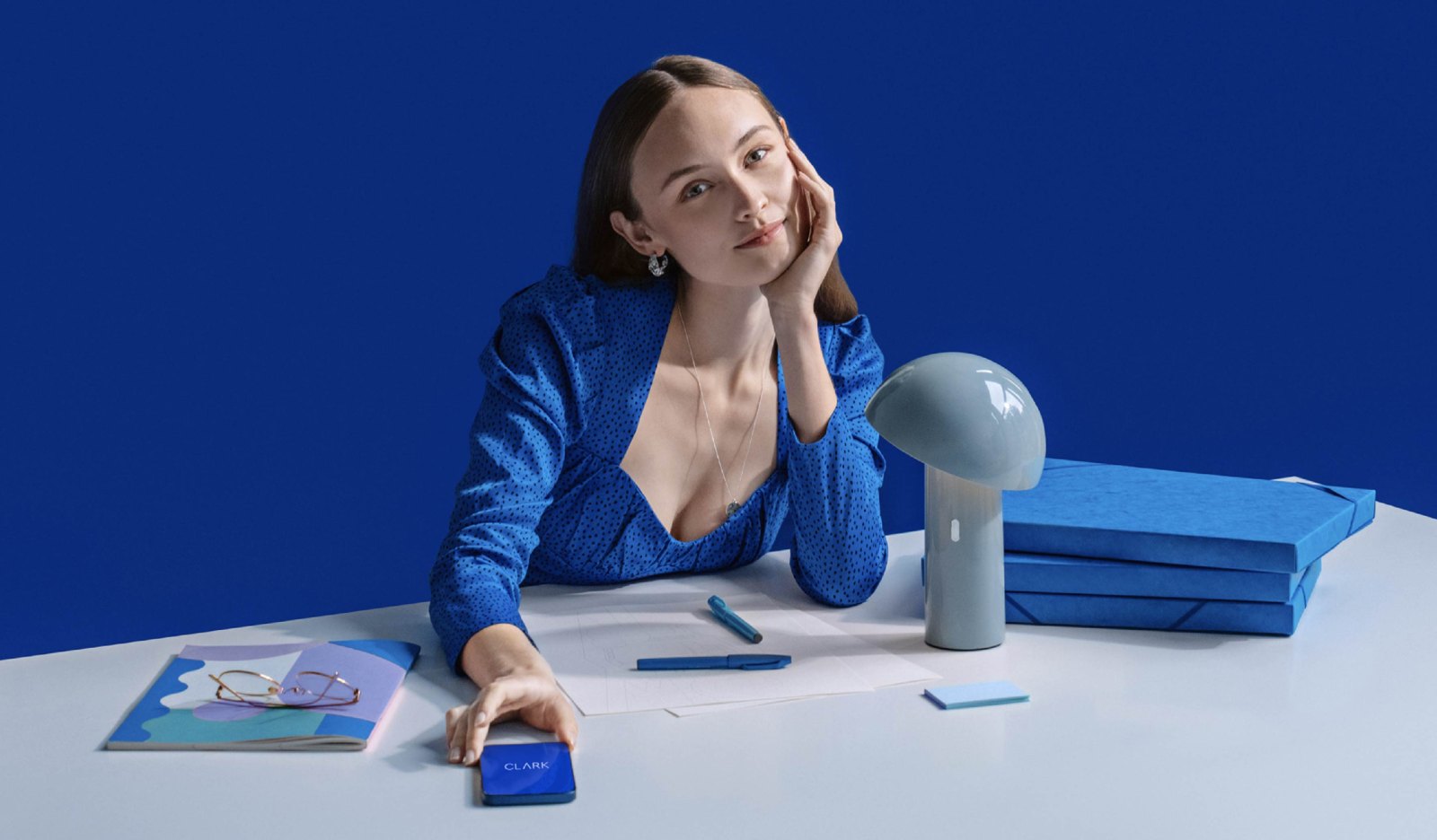 CLARK product photography — a woman at a blue-toned desk set with the app