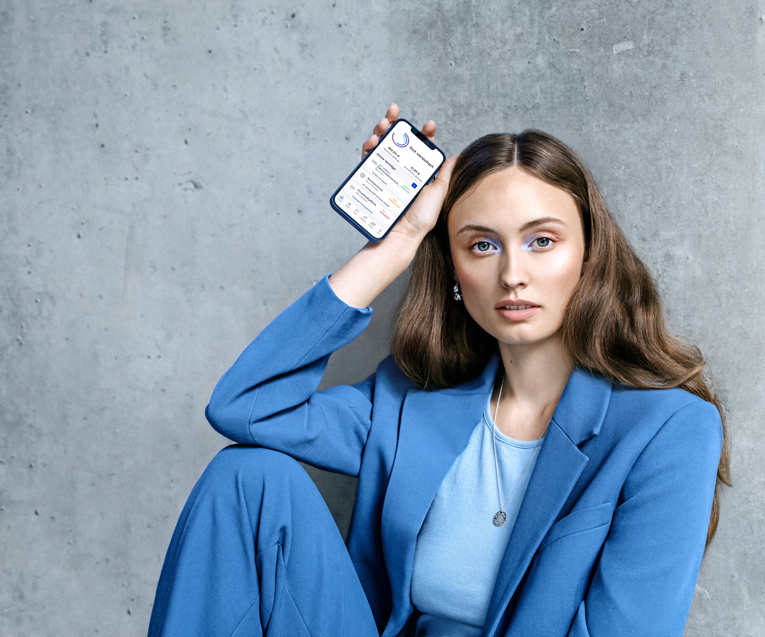 CLARK product photography — a model in a monochromatic blue suit seated against concrete, holding a phone with the CLARK app